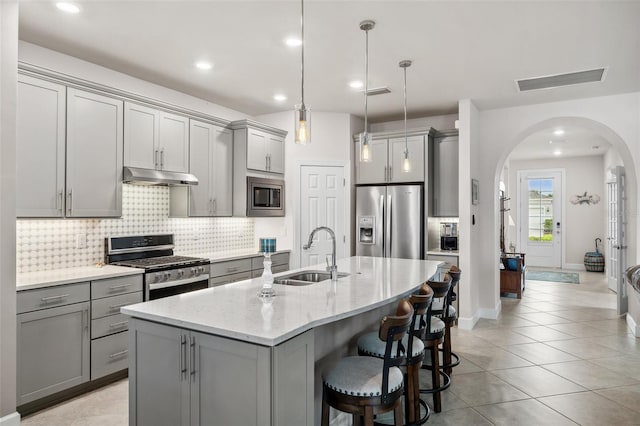 kitchen featuring gray cabinetry, hanging light fixtures, stainless steel appliances, sink, and light stone counters