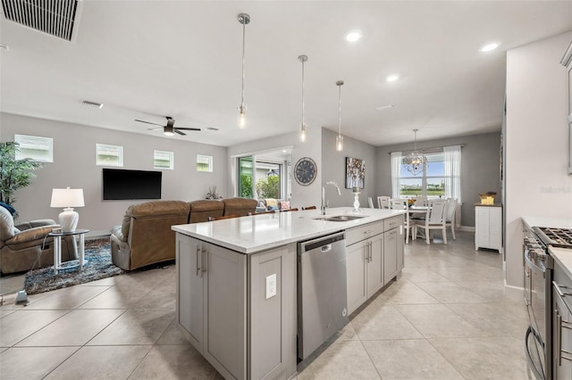 kitchen featuring an island with sink, gray cabinetry, decorative light fixtures, sink, and appliances with stainless steel finishes