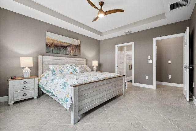 tiled bedroom featuring a tray ceiling, ceiling fan, and ensuite bath