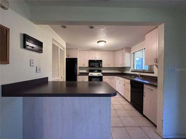 kitchen with dark countertops, a peninsula, black appliances, and a sink