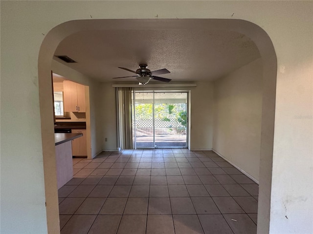 empty room featuring visible vents, a ceiling fan, a textured ceiling, arched walkways, and light tile patterned floors