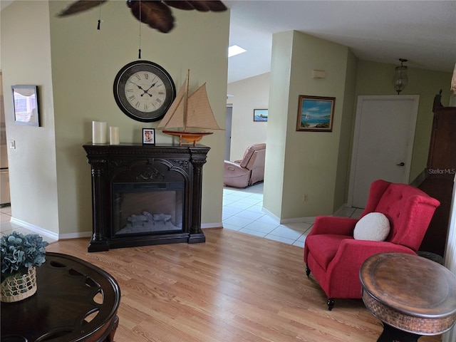 living area featuring light wood-style floors, lofted ceiling, a glass covered fireplace, and baseboards