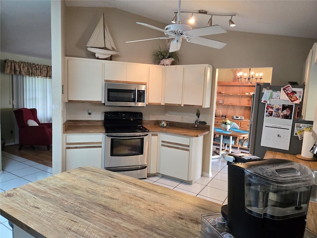 kitchen with lofted ceiling, appliances with stainless steel finishes, light tile patterned flooring, and white cabinets