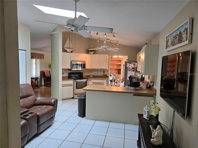 kitchen with light tile patterned floors, lofted ceiling with skylight, open floor plan, a peninsula, and stainless steel appliances