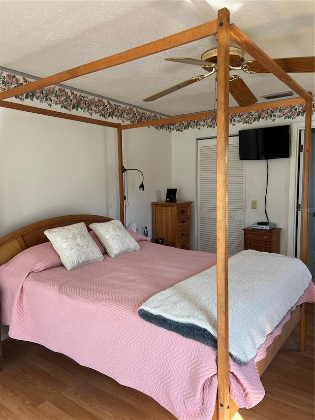 bedroom featuring a ceiling fan, a textured ceiling, visible vents, and wood finished floors