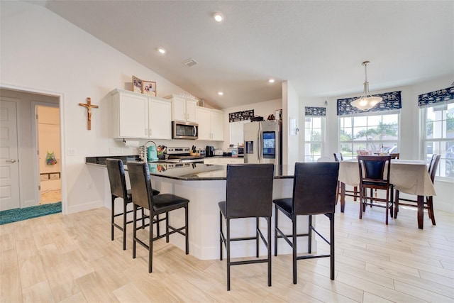 kitchen with lofted ceiling, pendant lighting, a kitchen breakfast bar, stainless steel appliances, and white cabinets