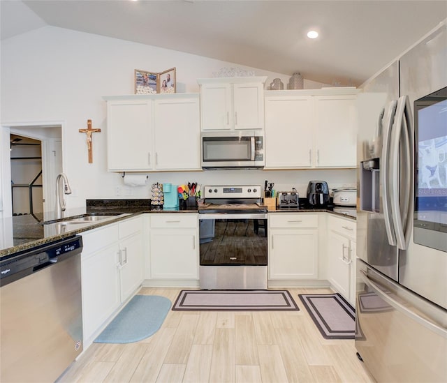 kitchen featuring white cabinetry, lofted ceiling, stainless steel appliances, sink, and dark stone countertops