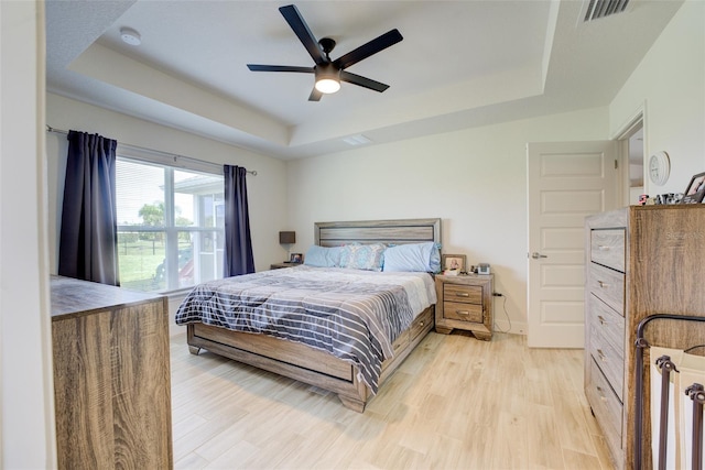 bedroom featuring ceiling fan, light hardwood / wood-style flooring, and a raised ceiling