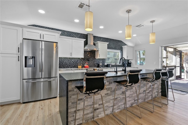 kitchen with wall chimney exhaust hood, white cabinetry, hanging light fixtures, and stainless steel refrigerator with ice dispenser