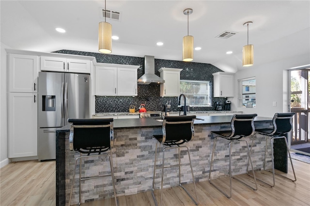 kitchen with a kitchen breakfast bar, wall chimney range hood, stainless steel fridge with ice dispenser, and hanging light fixtures