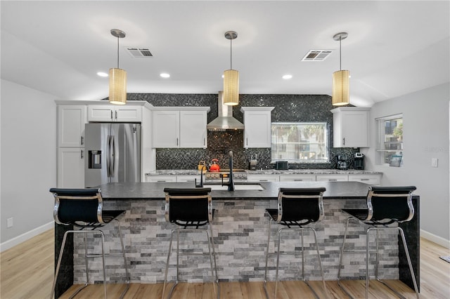 kitchen featuring a center island with sink, white cabinets, a breakfast bar area, and stainless steel refrigerator with ice dispenser