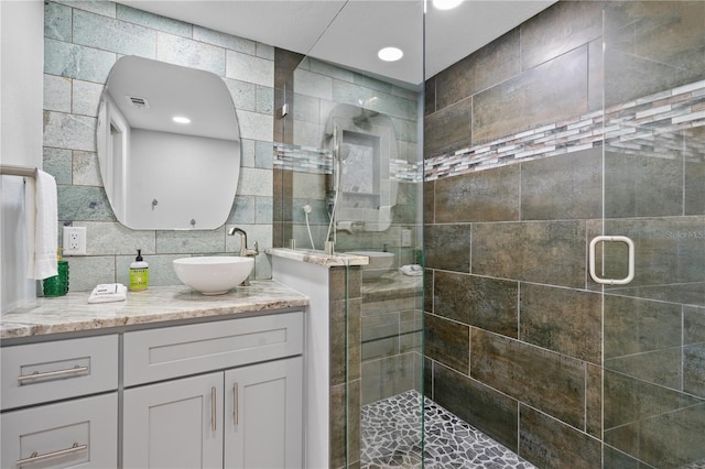 bathroom with tile walls, decorative backsplash, vanity, and walk in shower