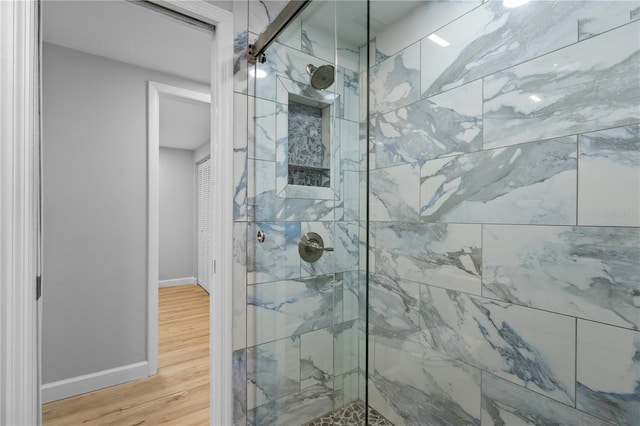 bathroom with tiled shower and wood-type flooring