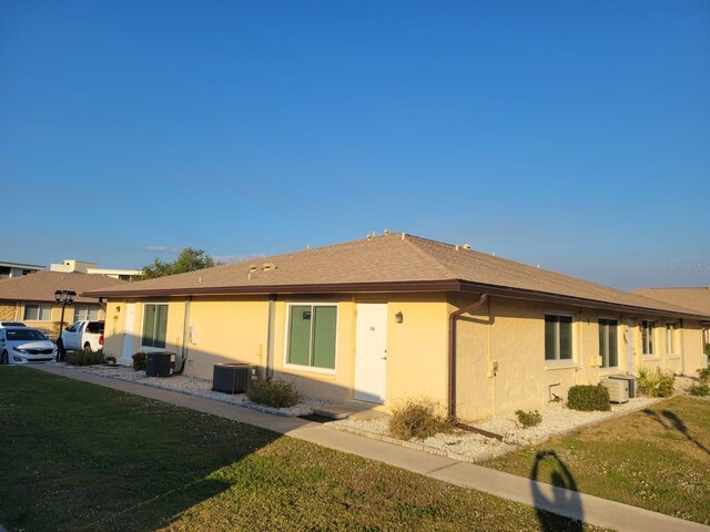 back of house featuring central air condition unit, a lawn, a shingled roof, and stucco siding