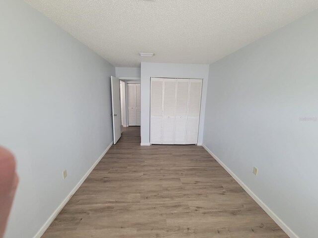 unfurnished bedroom with a closet, baseboards, a textured ceiling, and light wood finished floors