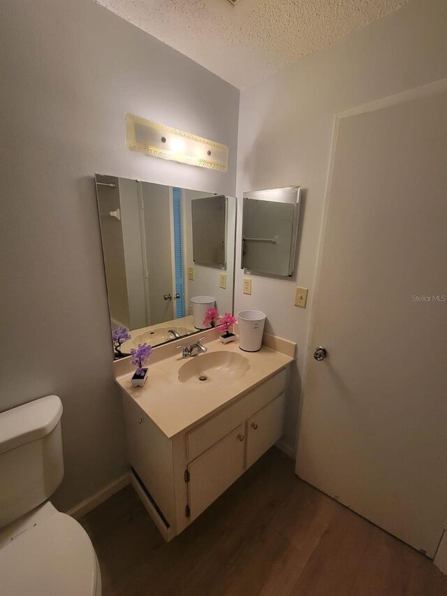 bathroom with toilet, vanity, a textured ceiling, and wood finished floors