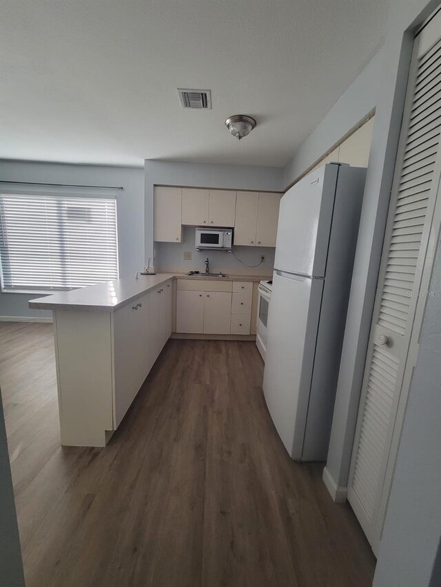 kitchen with white appliances, visible vents, dark wood-style floors, light countertops, and a sink