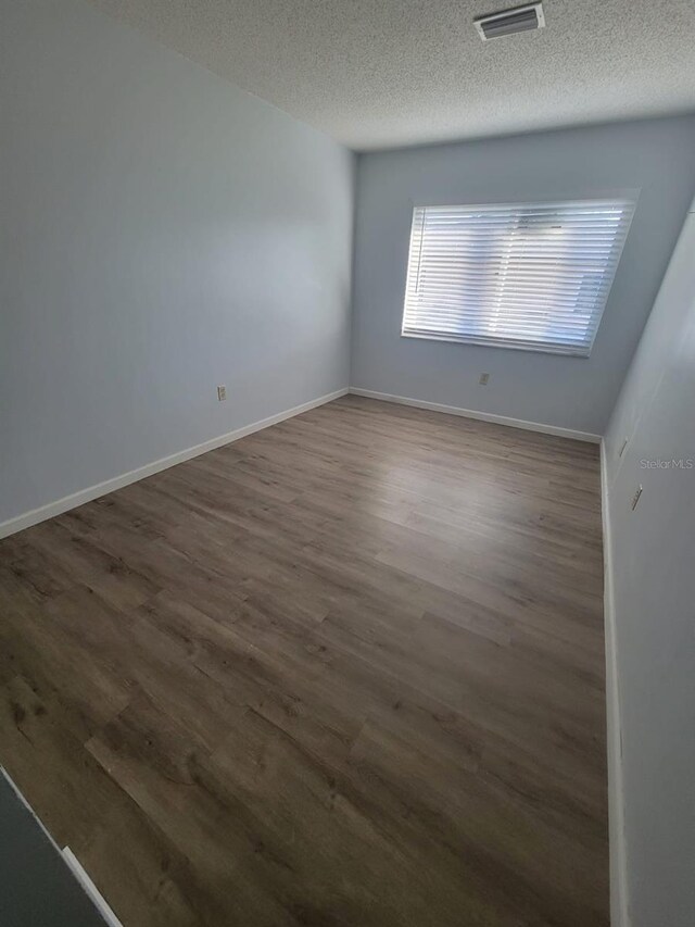 unfurnished room featuring dark wood-style floors, a textured ceiling, visible vents, and baseboards