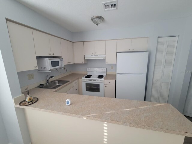 kitchen featuring light countertops, white cabinets, a sink, white appliances, and a peninsula