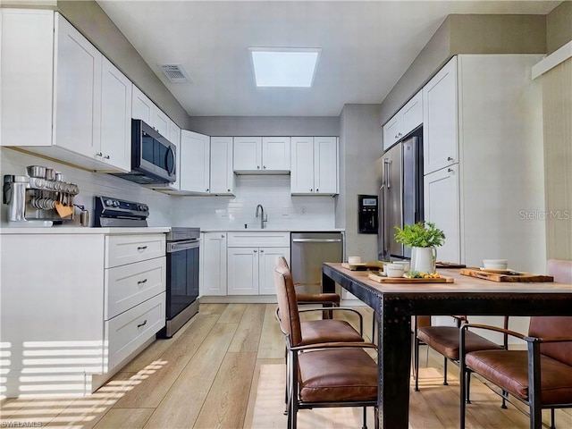 kitchen featuring visible vents, appliances with stainless steel finishes, light wood-style floors, white cabinetry, and a sink