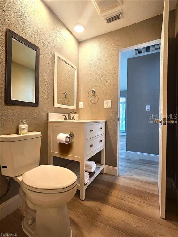 bathroom featuring toilet, a textured wall, wood finished floors, and visible vents