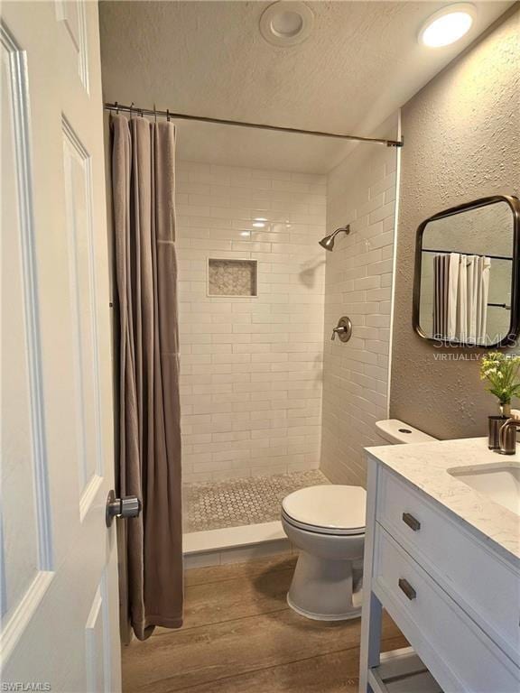 full bath featuring a textured wall, toilet, wood finished floors, a tile shower, and a textured ceiling