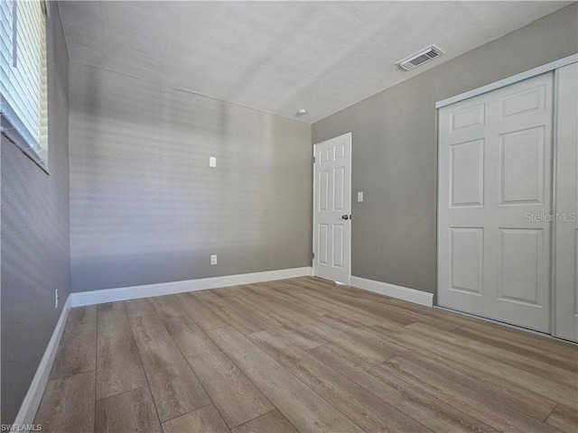 unfurnished bedroom featuring a closet, visible vents, baseboards, and wood finished floors