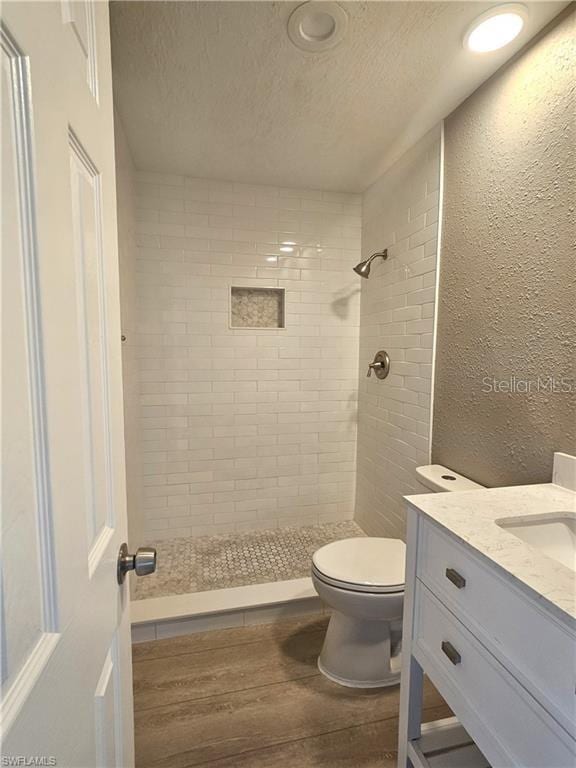 full bath featuring a textured wall, toilet, wood finished floors, a tile shower, and a textured ceiling