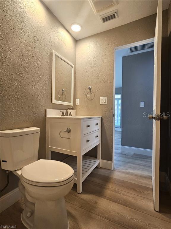 half bathroom featuring baseboards, visible vents, a textured wall, toilet, and wood finished floors