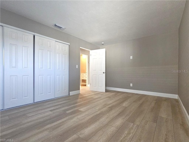 unfurnished bedroom with a closet, visible vents, baseboards, and wood finished floors