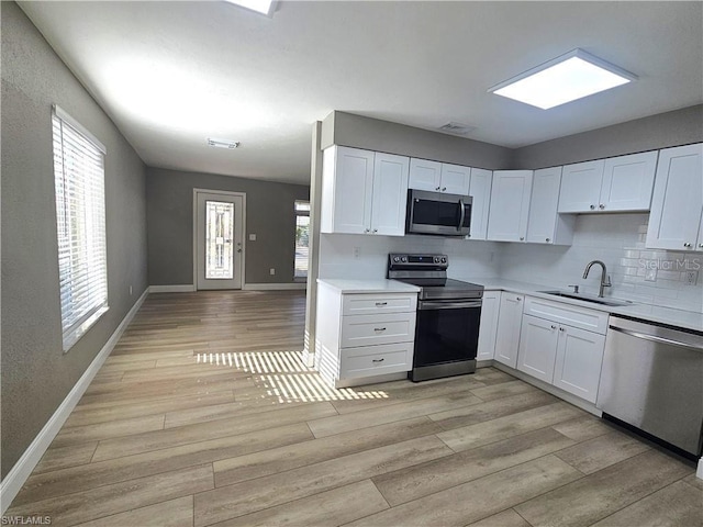 kitchen with a sink, white cabinetry, light countertops, appliances with stainless steel finishes, and light wood finished floors