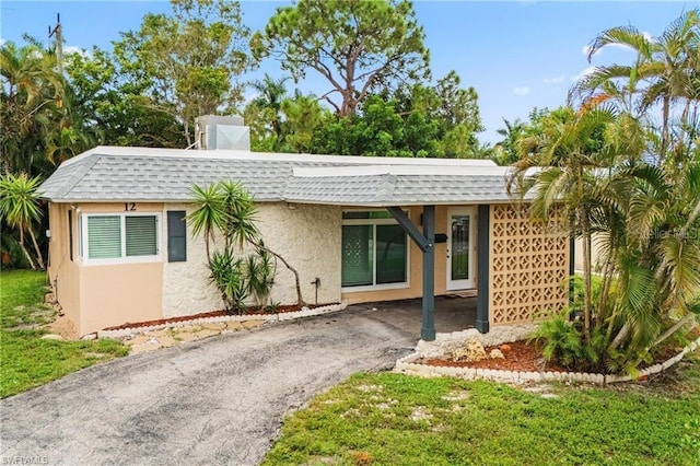 view of front of house featuring a shingled roof, aphalt driveway, mansard roof, and stucco siding