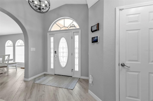 foyer entrance with arched walkways, light wood-type flooring, an inviting chandelier, and baseboards