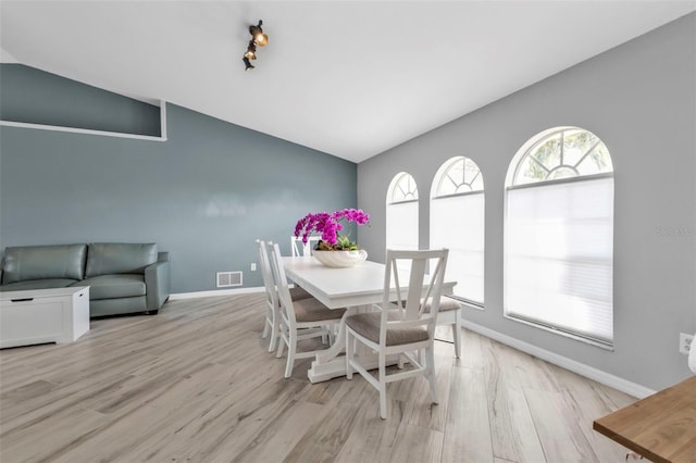 dining room with lofted ceiling, light wood finished floors, visible vents, and baseboards