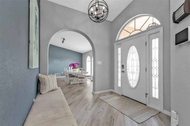 entryway featuring light wood-style floors, arched walkways, plenty of natural light, and an inviting chandelier