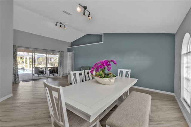 dining area featuring light wood-style flooring, visible vents, baseboards, vaulted ceiling, and rail lighting