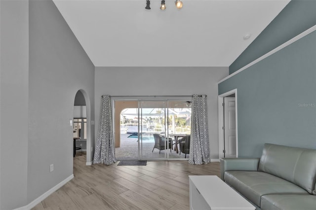 unfurnished living room featuring arched walkways, high vaulted ceiling, light wood-style flooring, and baseboards