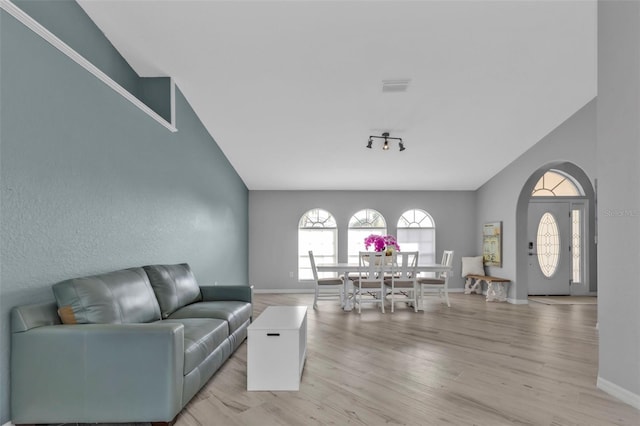 living room with arched walkways, light wood-style flooring, visible vents, baseboards, and vaulted ceiling