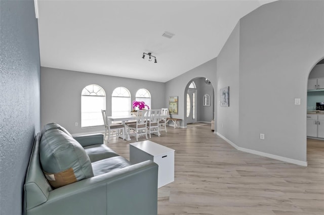 living room featuring arched walkways, lofted ceiling, visible vents, light wood-type flooring, and baseboards