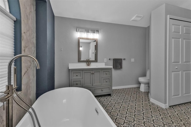 full bath with toilet, visible vents, vanity, a freestanding bath, and baseboards