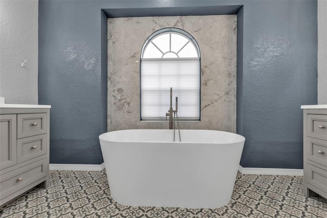 full bathroom with a soaking tub, a textured wall, vanity, and baseboards