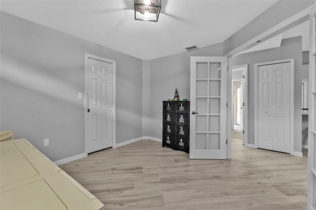 interior space with light wood-style flooring, visible vents, baseboards, and a textured ceiling