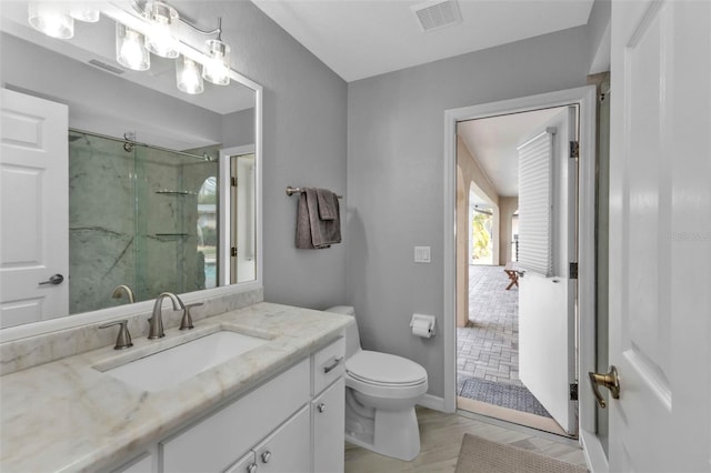 bathroom with a marble finish shower, visible vents, toilet, wood finished floors, and vanity