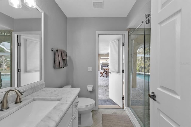 bathroom with toilet, wood finished floors, vanity, visible vents, and a shower stall