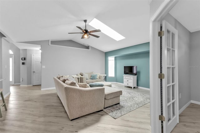 living room featuring ceiling fan, lofted ceiling with skylight, light wood-type flooring, and baseboards