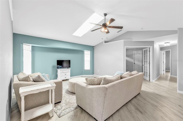 living room with vaulted ceiling with skylight, light wood-style flooring, visible vents, baseboards, and a ceiling fan