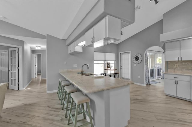 kitchen featuring a peninsula, a sink, visible vents, white cabinetry, and a kitchen bar