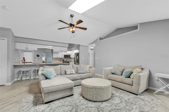 living room with light wood-style floors, vaulted ceiling with skylight, baseboards, and a ceiling fan