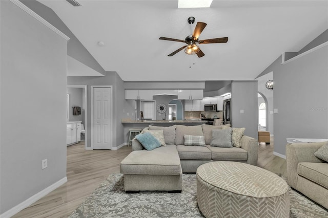 living area featuring arched walkways, vaulted ceiling, light wood-style flooring, and ceiling fan