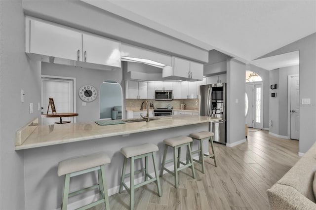 kitchen featuring white cabinets, a kitchen breakfast bar, a peninsula, stainless steel appliances, and a sink